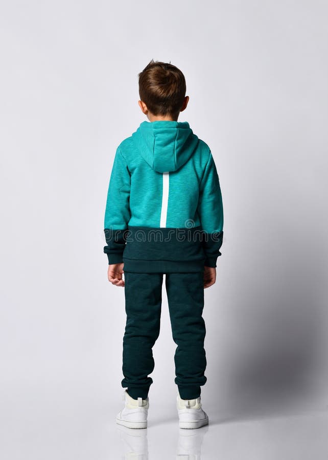 Portrait boy in warm tracksuit, sneakers back view. Portrait of little preschool or school boy wearing warm green black tracksuit with hood and white sneakers stock photos Portrait boy in warm tracksuit, sneakers back view. Portrait of little preschool or school boy wearing warm green black tracksuit with hood and white sneakers stock photos