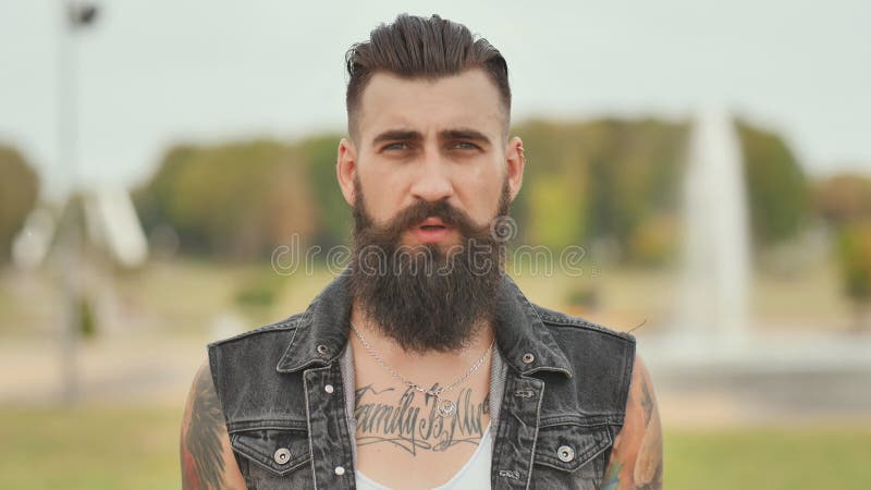 Portrait of a brutal and bearded man with tattoos on his shoulders.