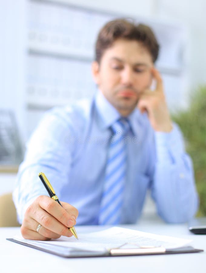 Portrait of a business man filling a form, focus on hand holding the pen