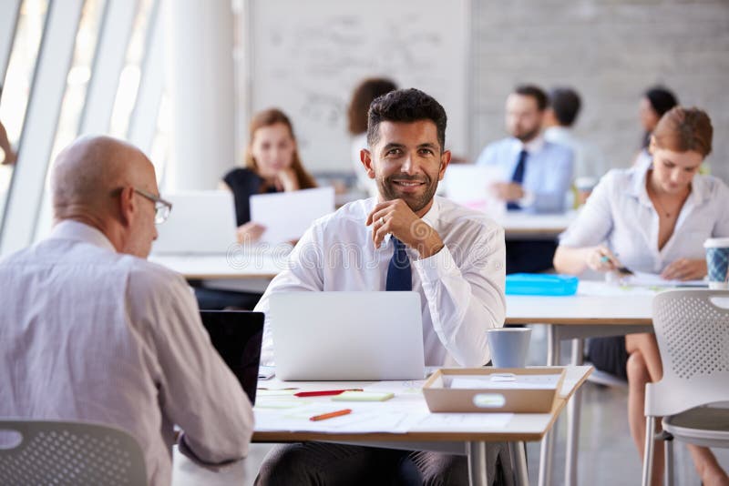 Portrait Of Businessman Working On Laptop In Busy Office