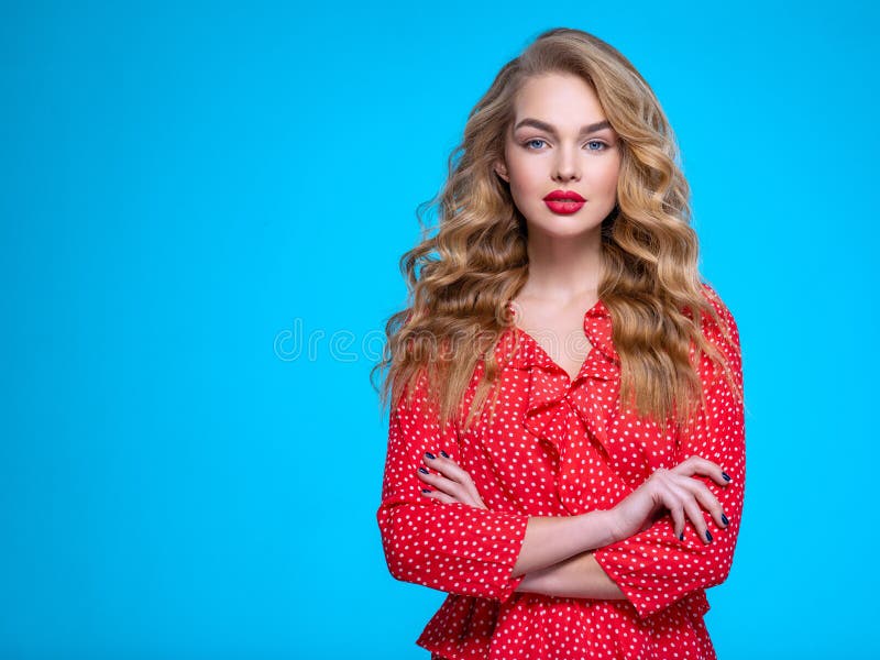 Portrait of a calm young blonde. Beautiful girl with long white hair. Model in a red shirt poses in studio. People with crossed