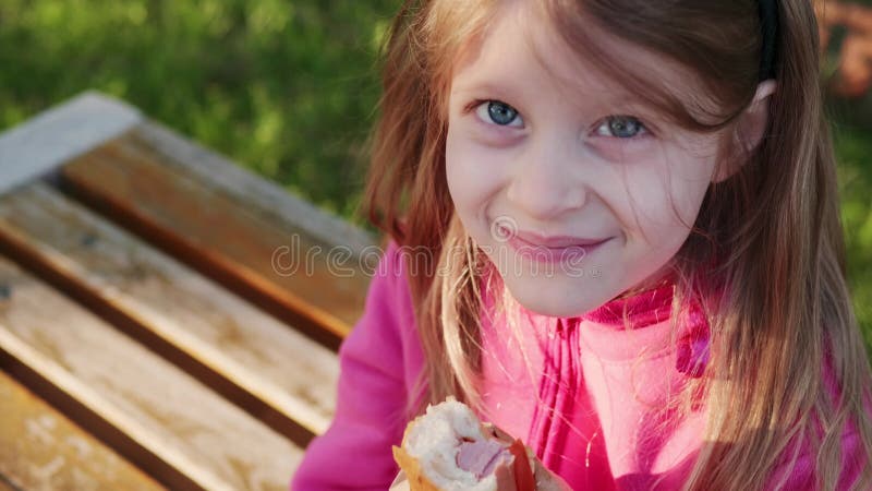 cute child in a pink jacket eating a hot dog outdoors