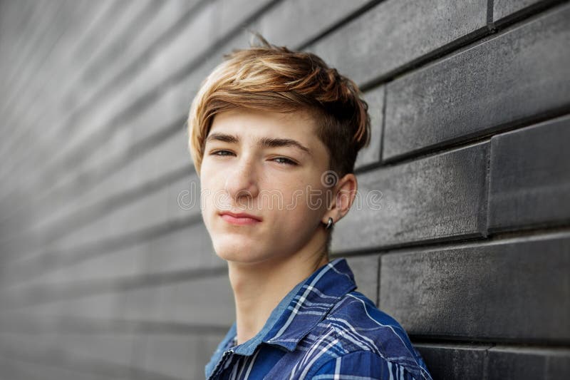 Portrait of caucasian young man teenager looking at the camera. Gray wall. Urban people style. Gen Z