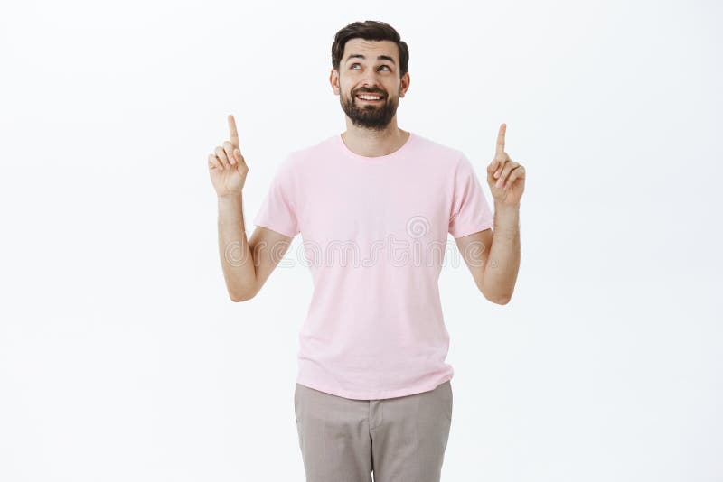 Portrait of charming carefree and delighted male model with dark beard smiling happily looking and pointing up enjoying royalty free stock photo Portrait of charming carefree and delighted male model with dark beard smiling happily looking and pointing up enjoying royalty free stock photo