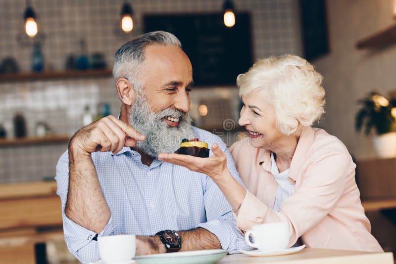 Portrait of Cheerful Elderly Couple Sitting at Table with Cups of