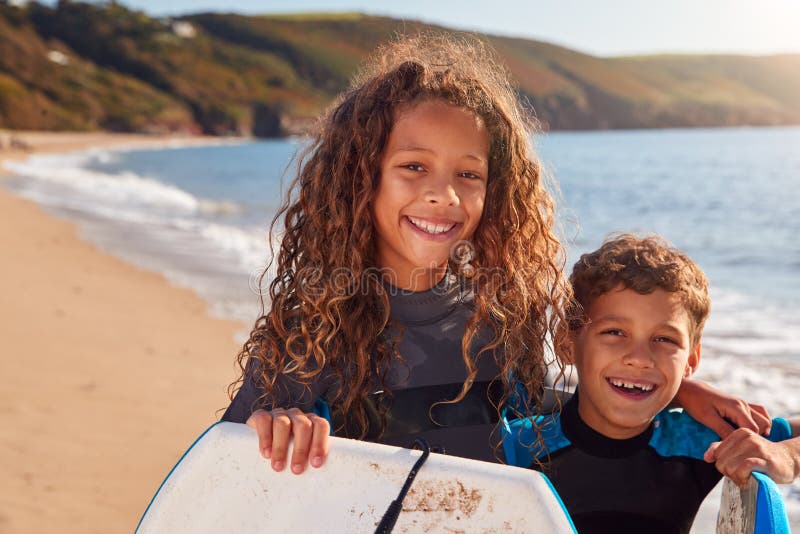 Portrait Of Children Wearing Wetsuits Holding Bodyboards On Summer Beach Vacation Having Fun By Sea royalty free stock photo