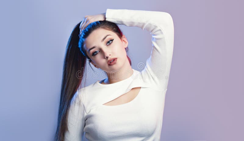 Portrait of cocky girl with long ponytail hair on studio background, young woman with rebellious character, fashion model
