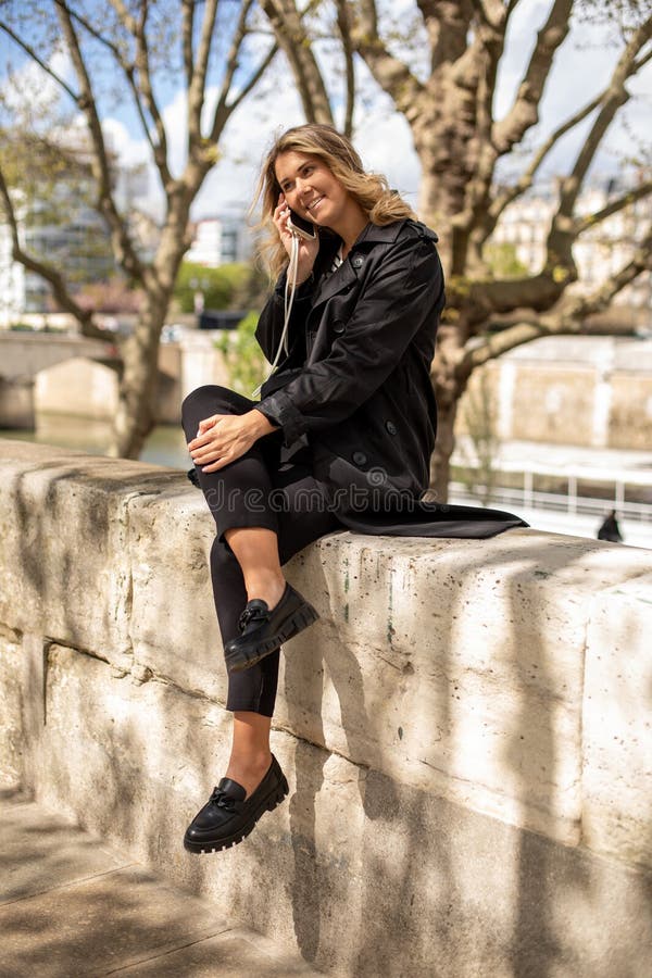 Portrait complet d'une femme d'affaires assise sur un parapet de pierre parlant au téléphone le jour du printemps. image stock