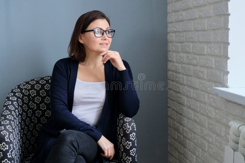 Portrait Of A Confident Mature Woman With Glasses Sitting In A Chair