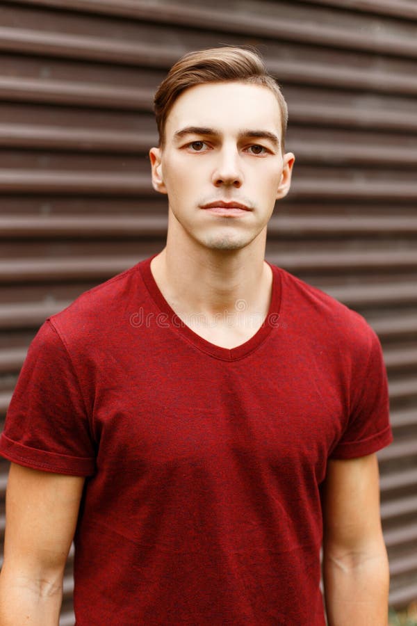 Portrait of a cool handsome young man in a fashionable red t-shirt with a stylish hairstyle near a vintage metal building. royalty free stock photography Portrait of a cool handsome young man in a fashionable red t-shirt with a stylish hairstyle near a vintage metal building. royalty free stock photography
