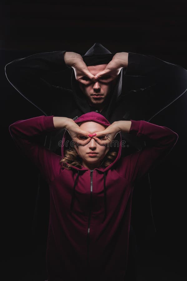 Portrait of a couple of men and women in hoods in a dark room covering their faces with masks from their palms. Symbol of organized crime and robbery hackers. Portrait of a couple of men and women in hoods in a dark room covering their faces with masks from their palms. Symbol of organized crime and robbery hackers.