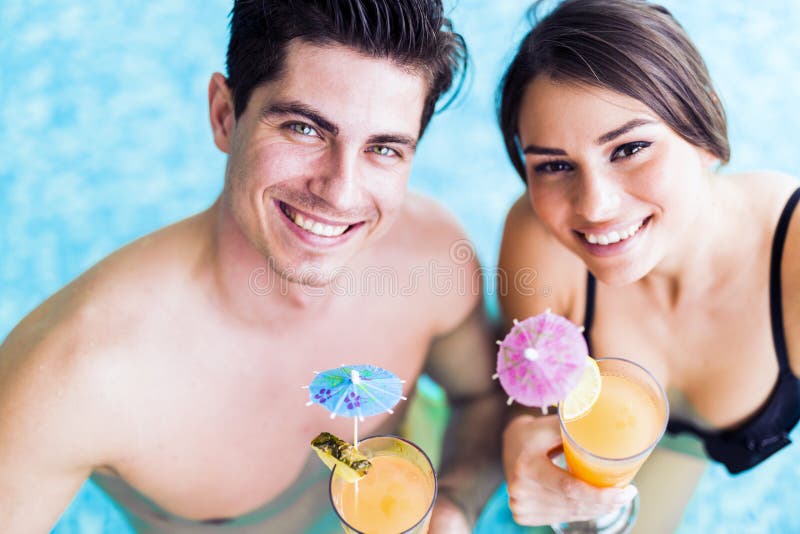 Portrait Of A Couple Smiling And Drinking A Cocktail In A Pool Stock