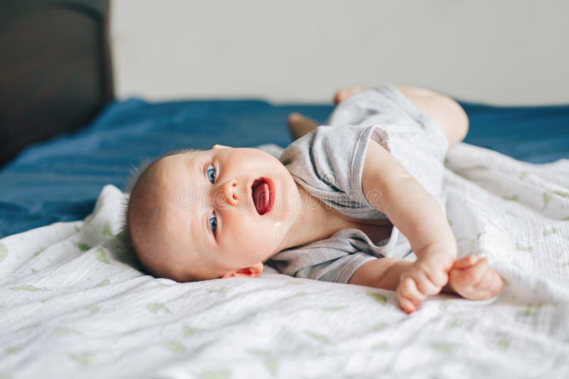 Portrait of crying screaming drooling white Caucasian baby girl boy four months old lying on bed in bedroom on tummy. Natural emotion expression. Childhood lifestyle. Portrait of crying screaming drooling white Caucasian baby girl boy four months old lying on bed in bedroom on tummy. Natural emotion expression. Childhood lifestyle