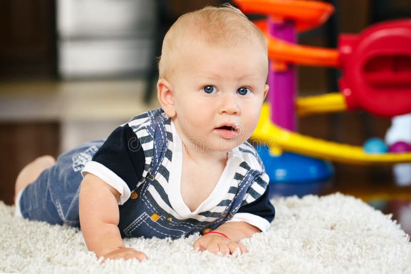 Portrait of cute adorable blond Caucasian smiling baby boy with blue eyes lying on floor in kids children room