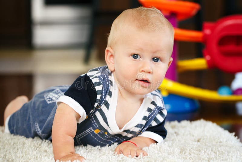 Portrait of cute adorable blond Caucasian smiling baby boy with blue eyes lying on floor in kids children room