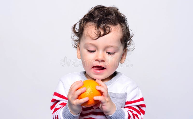 Portrait of a cute baby craving an orange.