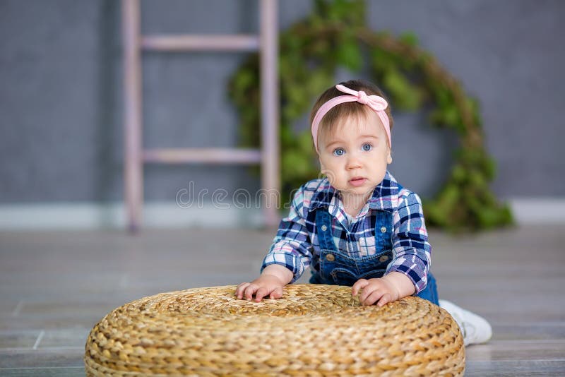Portrait of a cute baby girl on a light background with a wreath of flowers on her head sitting on sofa basket