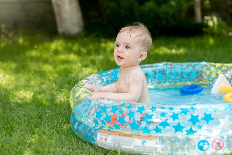 Portrait of cute baby having fun in inflatable swimming pool at hot summer day