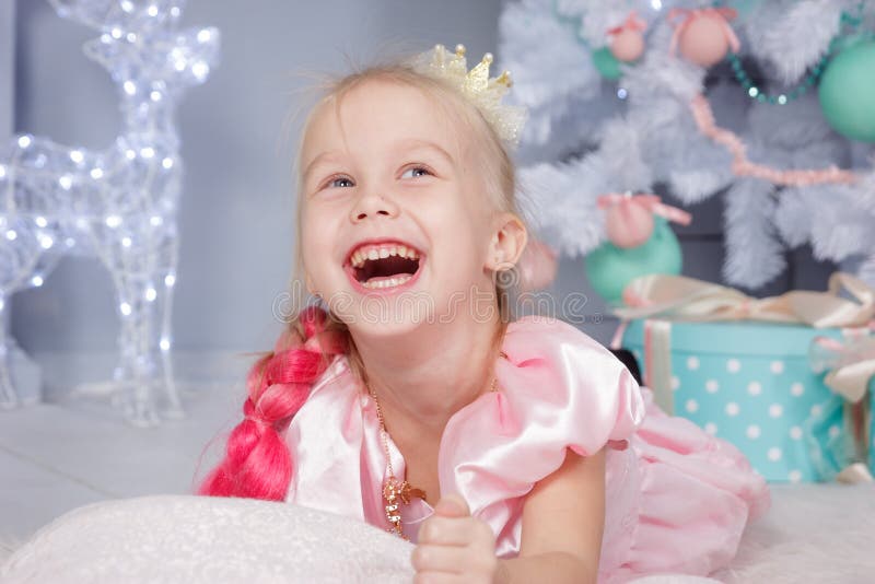 Portrait of cute european little blonde princess girl with crown in beautiful dress in decorated studio in christmas location with