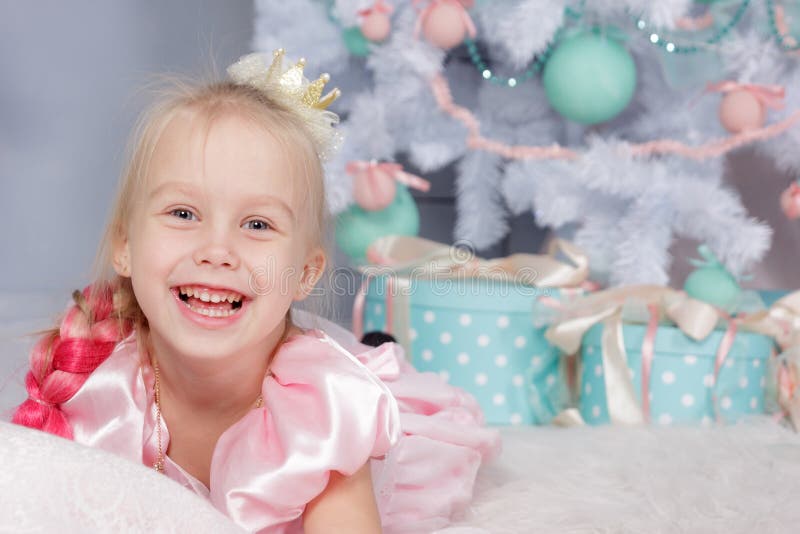 Portrait of cute european little blonde princess girl with crown in beautiful dress in decorated studio in christmas location with