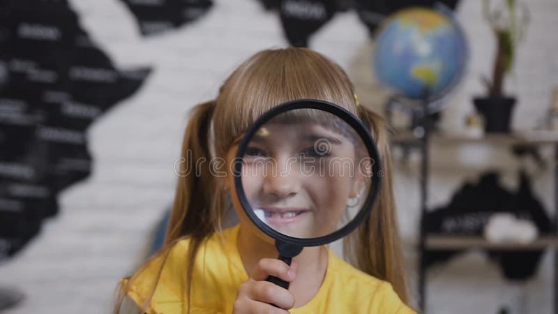 Portrait of a cute girl who playing looking in magnifying glass. Close-up. A beautiful girl looks into camera and smiles
