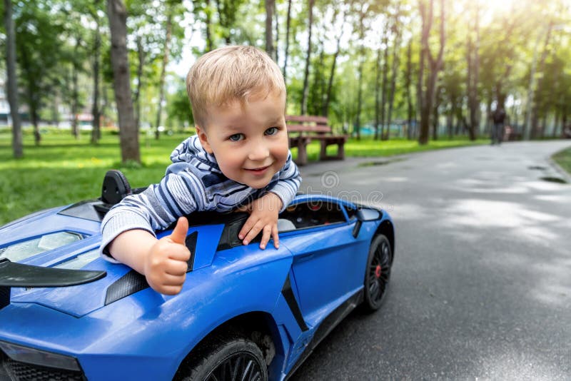 Portrait of cute little caucasain blond toddler boy enjoy having fun riding electric powered toy car by asphalt path