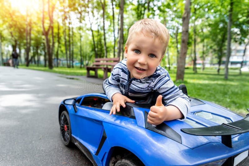 Portrait of cute little caucasain blond toddler boy enjoy having fun riding electric powered toy car by asphalt path