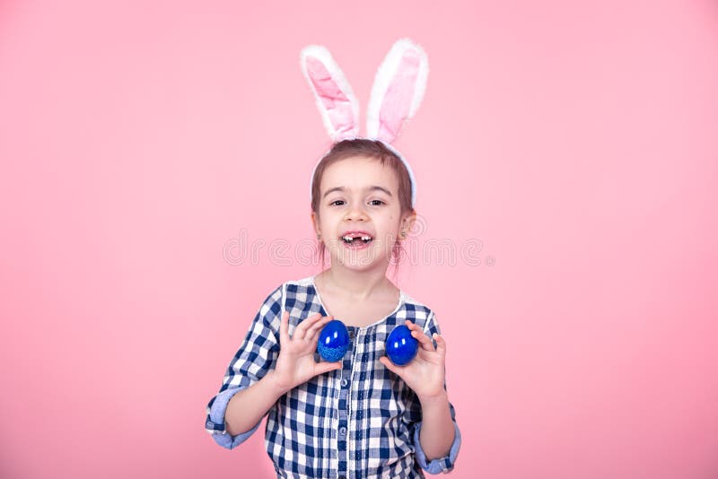 Portrait of a cute little girl with Easter eggs on a pink background