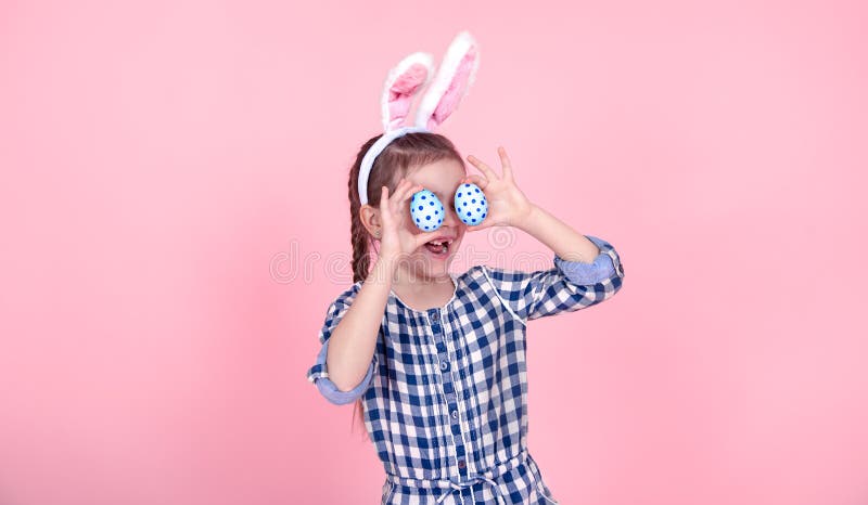 Portrait of a cute little girl with Easter eggs on a pink background