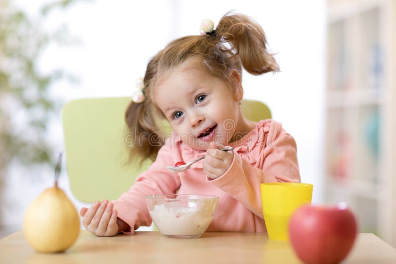Portrait of cute little girl eating fruits and yogurt for breakfast at home