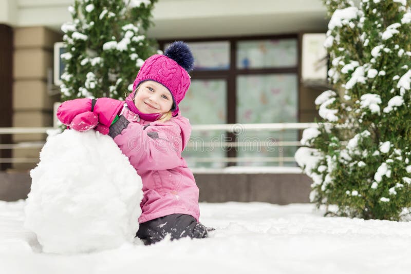 Portrait of cute little girl making smowman. at bright winter day. Adorable child playing with snow outdoors. Funny