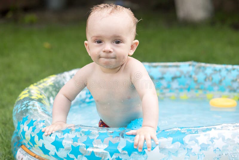 Portrait of cute 10 months old baby boy enjoying swimming in inflatable pool