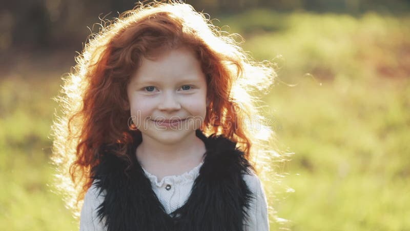 Portrait of cute redhead little girl walking in an autumn park. Slow motion. Autumn Park. Young little girl is smiling