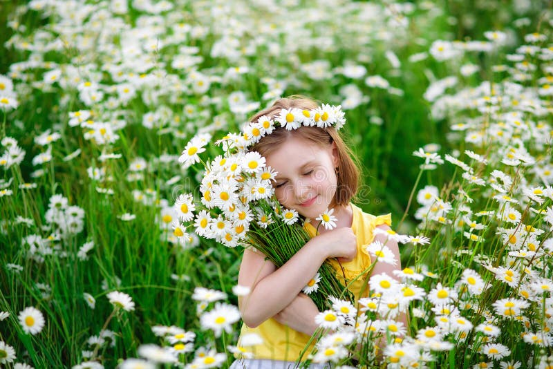 Portrait of a cute village girl in a wreath and a bouquet of flowers on a chamomile field. A child in a blooming daisy meadow. She