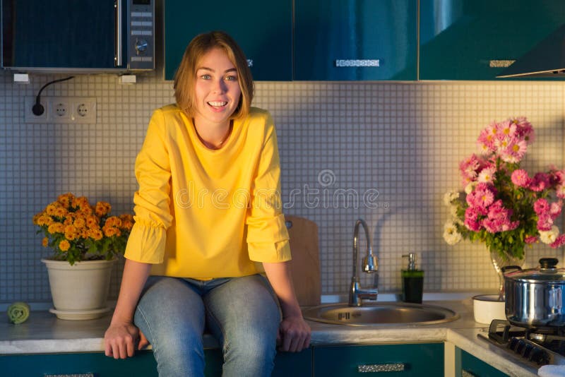 Portrait of cute yong woman sitting on kitchen countertops and cute smiling stock photos Portrait of cute yong woman sitting on kitchen countertops and cute smiling stock photos