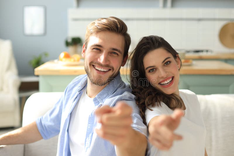 Portrait of cute young couple pointing and laughing, sitting in sofa