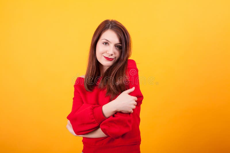 Portrait Of Cute Young Woman Gives Herself A Hug Over Yellow Background