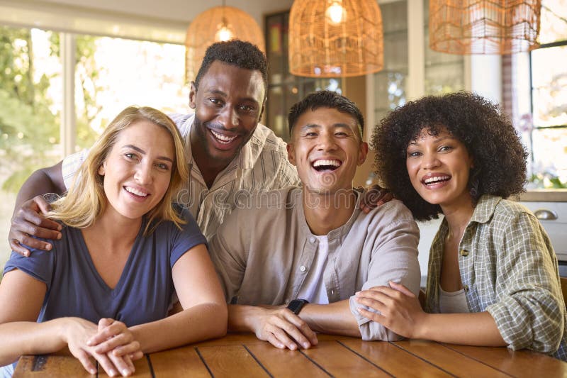 Portrait d'amis multiraciaux assis autour d'une table à la maison souriant ensemble devant la caméra photos libres de droits