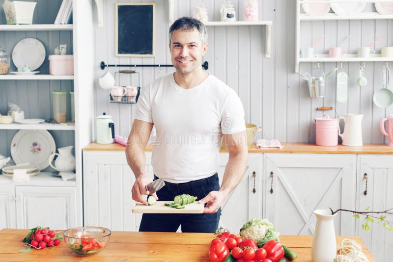Portrait d'homme de sourire bel à la cuisine cuisson et concept à la maison - fermez-vous de la main masculine coupant le concomb photo stock Portrait d'homme de sourire bel à la cuisine cuisson et concept à la maison - fermez-vous de la main masculine coupant le concomb photo stock