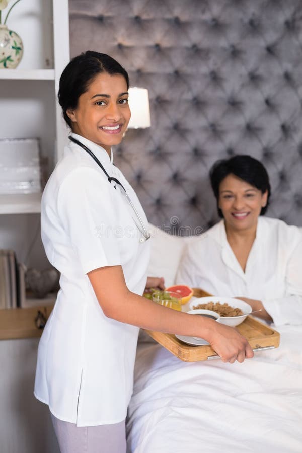 Portrait d'infirmière de sourire donnant le petit déjeuner au patient se reposant sur le lit