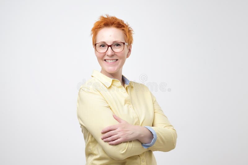 Portrait d'isolement de femme mûre de sourire avec le redhair court intéressant se tenant avec les bras croisés image stock Portrait d'isolement de femme mûre de sourire avec le redhair court intéressant se tenant avec les bras croisés image stock