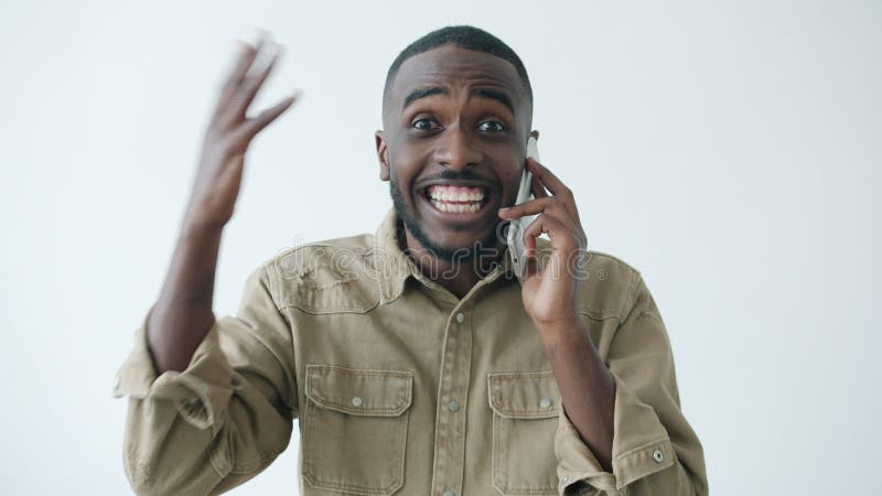 Portrait d'un afro-américain heureux en train de bavarder sur son téléphone portable et de faire des gestes sur fond blanc banque de vidéos