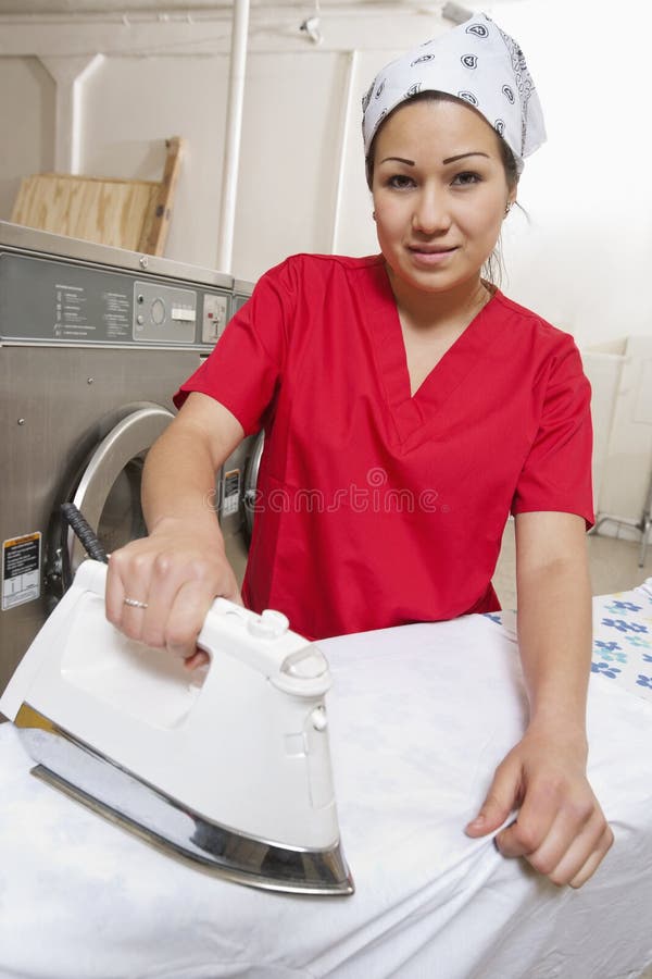 Portrait d'un bandana de port des employés féminins tout en repassant dans la laverie automatique photographie stock libre de droits Portrait d'un bandana de port des employés féminins tout en repassant dans la laverie automatique photographie stock libre de droits