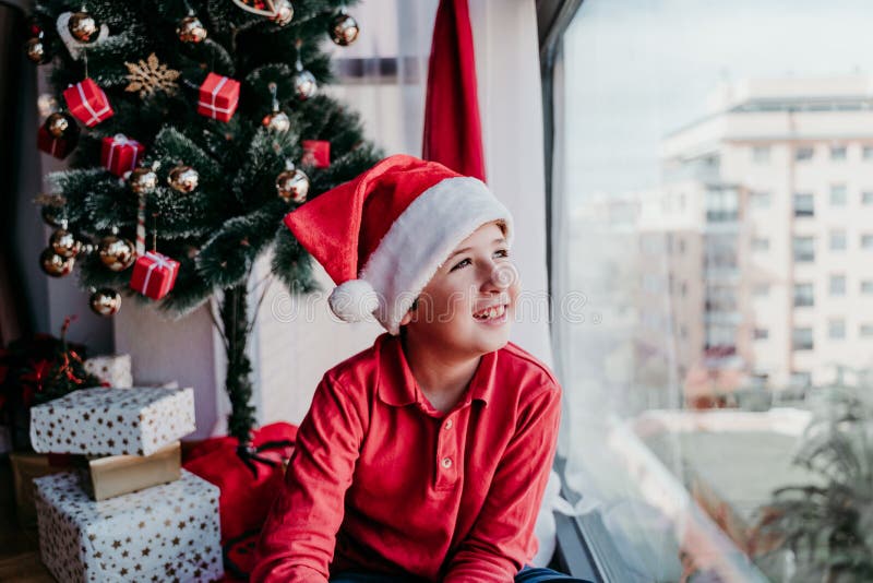 portrait d'un beau garçon à la maison assis près de l'arbre de noël et cadeaux en regardant par la fenêtre images libres de droits portrait d'un beau garçon à la maison assis près de l'arbre de noël et cadeaux en regardant par la fenêtre images libres de droits