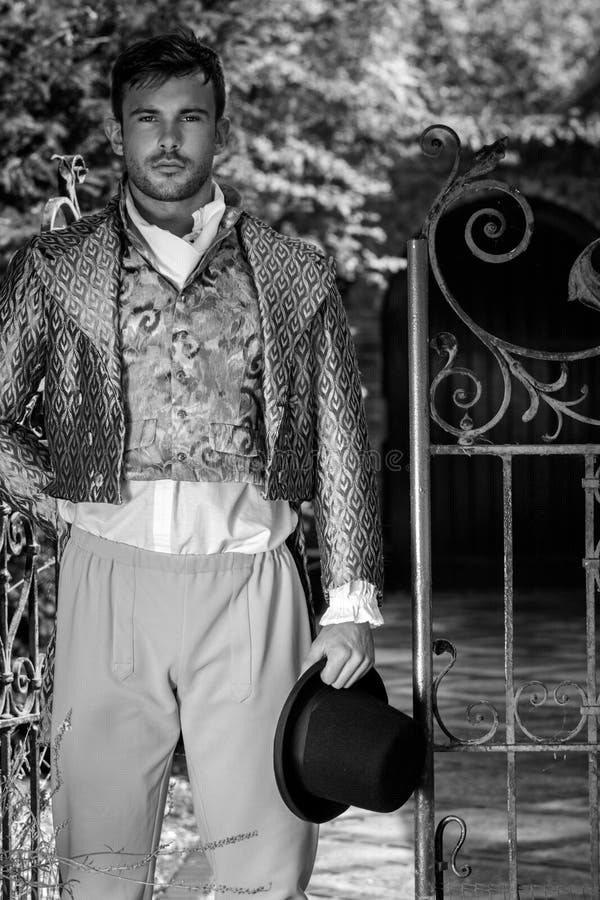 Portrait d'un bel homme vêtu de costumes vintage, tenant son chapeau dans une cour à la maison imposante image stock Portrait d'un bel homme vêtu de costumes vintage, tenant son chapeau dans une cour à la maison imposante image stock