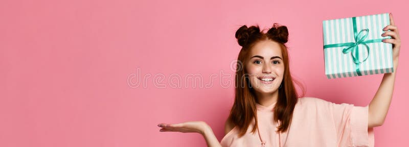Portrait d'un boîte-cadeau roux assez de sourire et de le regarder de participation de fille, d'isolement au-dessus du fond rose images libres de droits Portrait d'un boîte-cadeau roux assez de sourire et de le regarder de participation de fille, d'isolement au-dessus du fond rose images libres de droits