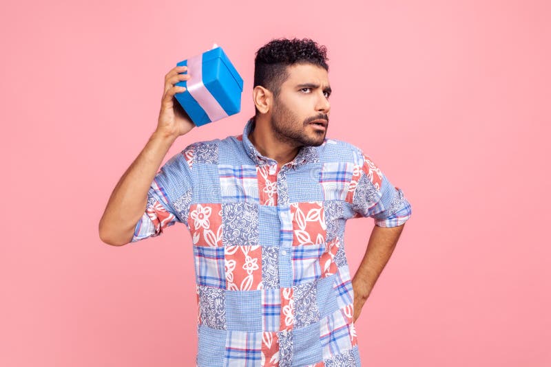 Portrait d'un curieux homme barbu portant un bleu casual style chemise tenant et secouant enveloppé boîte cadeau être intéressé ce photo libre de droits