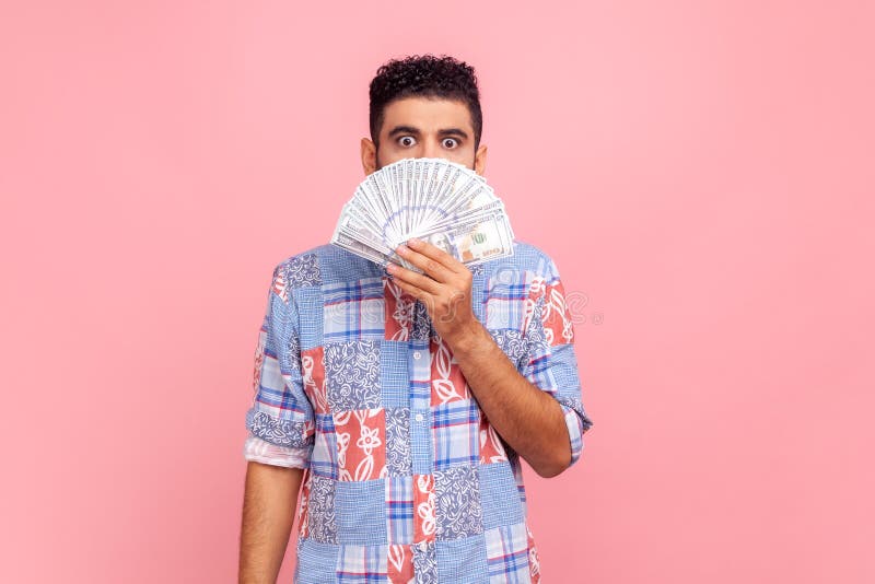 Portrait d'un homme attrayant surpris avec barbe vêtu d'une chemise casual bleue montrant de nombreux dollars en liquide couvrant photos stock