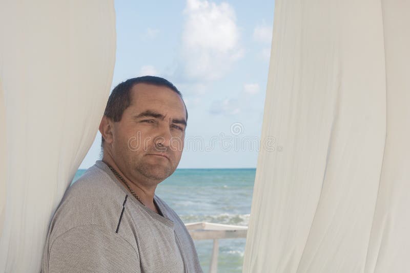 Portrait d'un homme à la fenêtre avec rideaux blancs. mer ou océan en arrière-plan photos libres de droits