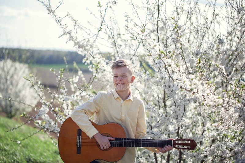 Portrait d'un jeune garçon de 11 ans tenant au printemps le parc et jouant la guitare image libre de droits Portrait d'un jeune garçon de 11 ans tenant au printemps le parc et jouant la guitare image libre de droits